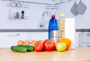 Taze çiğ sebze, domates, salatalık, yumurta, portakal, elma, bir şişe su ve yağ modern bir mutfak odasındaki ahşap bir masada süt. Sağlıklı beslenme. Organik gıda ve ürün teslimatı