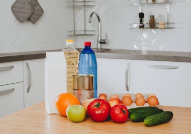 Taze çiğ sebze, domates, salatalık, yumurta, portakal, elma, bir şişe su ve yağ modern bir mutfak odasındaki ahşap bir masada süt. Sağlıklı beslenme. Organik gıda ve ürün teslimatı