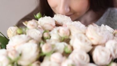 Beyaz kadın çiçek buketinin tadını çıkarıyor. Genç esmer kadın beyaz gülleri kokluyor çiçekleri kokluyor ve gülümsüyor..