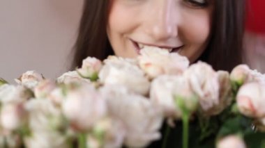 Beyaz kadın çiçek buketinin tadını çıkarıyor. Genç esmer kadın beyaz gülleri kokluyor çiçekleri kokluyor ve gülümsüyor..