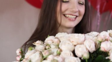 Beyaz kadın çiçek buketinin tadını çıkarıyor. Genç esmer kadın beyaz gülleri kokluyor çiçekleri kokluyor ve gülümsüyor..