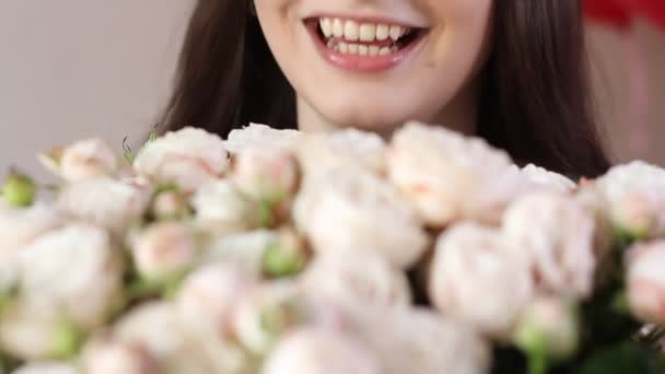 白人女性は花束を楽しむ 若いブルネットの女性は白いバラの花の香りと笑顔を嗅ぎます クローズアップビュー — ストック動画