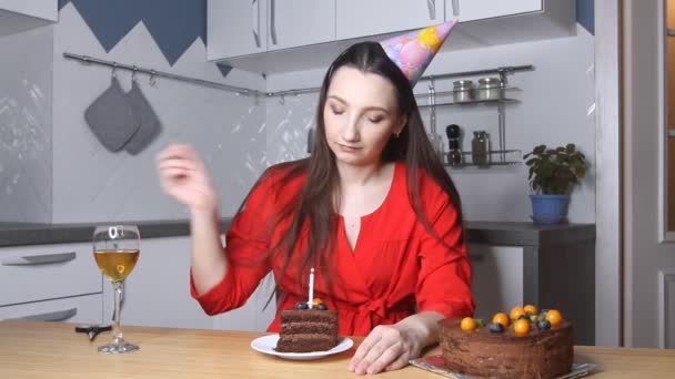 可悲的年轻女子戴着生日礼帽在厨房里单独庆祝生日 一个人坐着 点着蜡烛吃蛋糕 — 图库视频影像