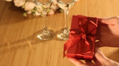 Erkek kadına kırmızı hediye kutusu ve kurdele verir. Kapalı bir restoranda ya da evde, romantik bir akşam yemeği. Sevgililer Günü, Uluslararası Kadınlar Günü, doğum günü, tatil konsepti.