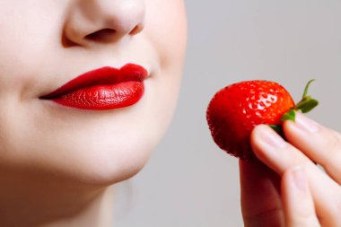 Makro, beyaz kadının dudaklarını kırmızı ruj ve taze çilekle kapat. Yemek zevki, sağlıklı gıda konsepti