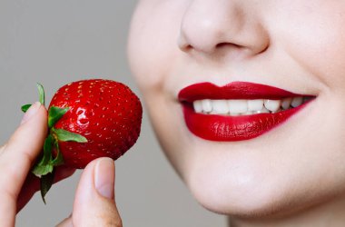 Makro, beyaz kadının dudaklarını kırmızı ruj ve taze çilekle kapat. Yemek zevki, sağlıklı gıda konsepti