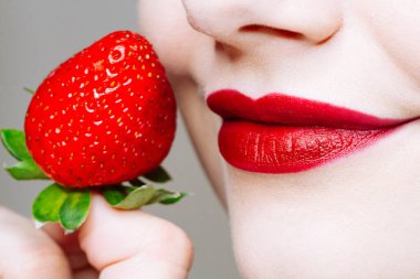 Makro, beyaz kadının dudaklarını kırmızı ruj ve taze çilekle kapat. Yemek zevki, sağlıklı gıda konsepti