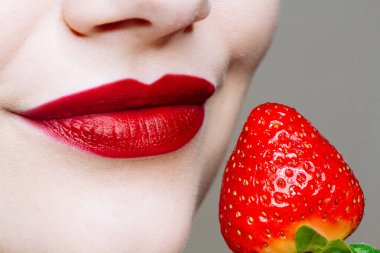 Makro, beyaz kadının dudaklarını kırmızı ruj ve taze çilekle kapat. Yemek zevki, sağlıklı gıda konsepti