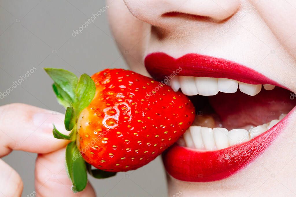 Macro close up of caucasus woman's lips with red lipstick and fresh strawberry. Food pleasure, healthy food concept