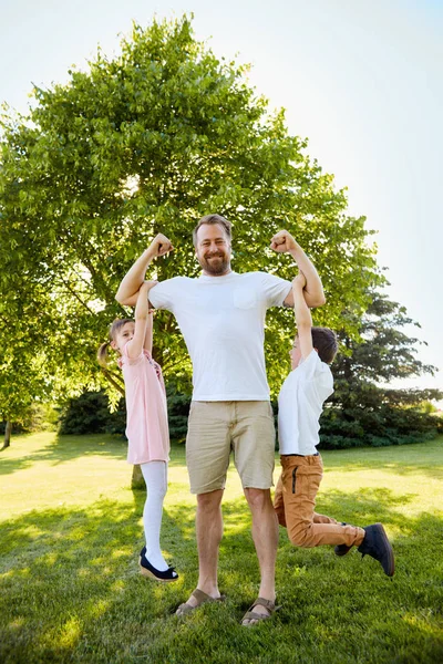 Glücklicher Junge und Mädchen hängen an den Muskeln des Vaters — Stockfoto