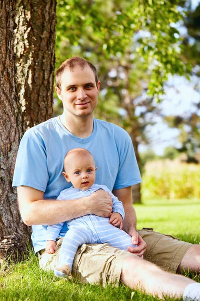 Père heureux assis avec le fils nouveau-né sur l'herbe — Photo