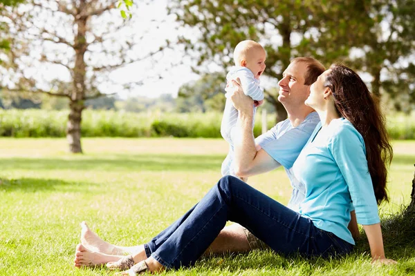 Parents heureux assis sur l'herbe tenant le fils nouveau-né — Photo