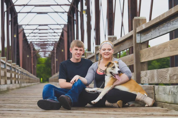 Feliz jovem casal posando na ponte com seu cão — Fotografia de Stock