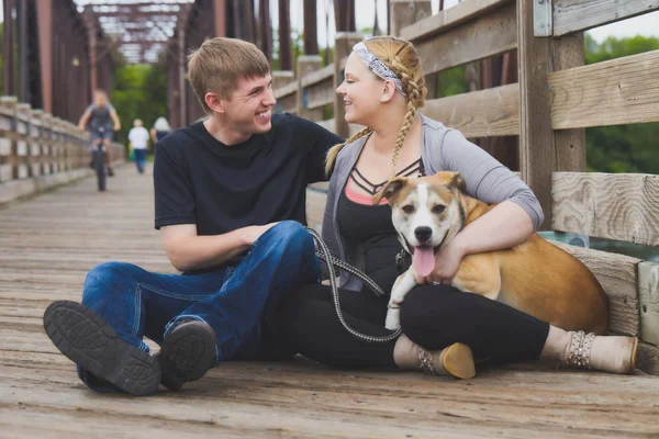 Feliz joven pareja sentada en el puente con el perro —  Fotos de Stock