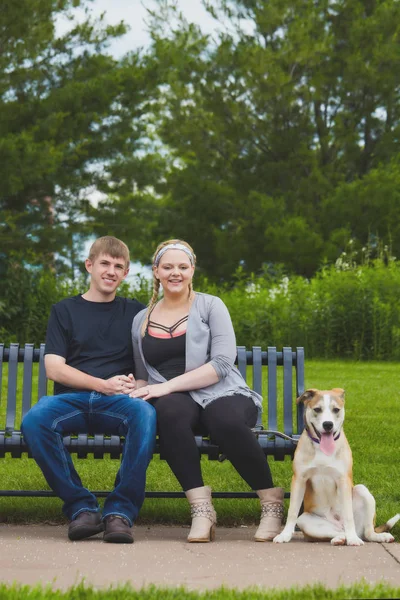 Casal feliz sentado no banco com cão na trela — Fotografia de Stock