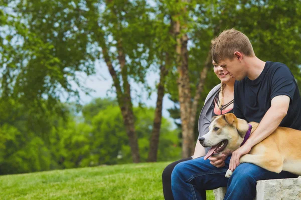 Sonriente pareja descansando sobre piedra con su perro —  Fotos de Stock