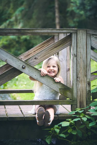 Portrait of happy little girl sitting on wooden bridge — Stock Photo, Image