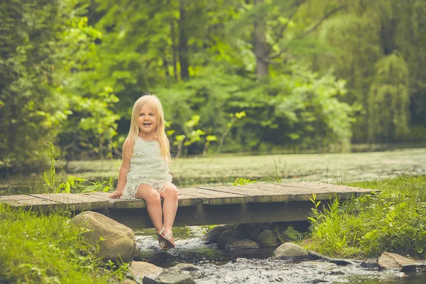 Niña feliz sentada en un puente de madera — Foto de Stock