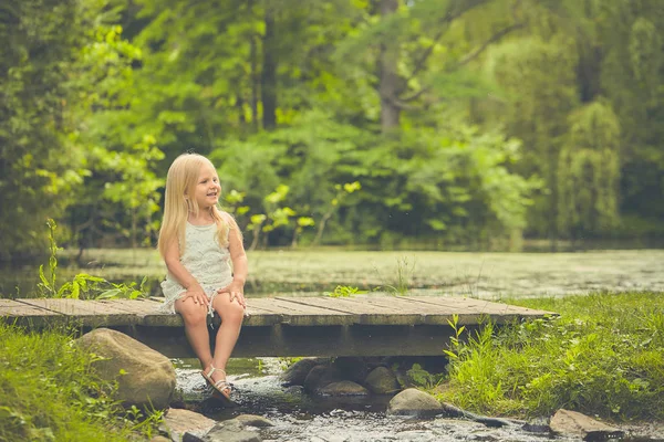 Little girl resting on wooden bridge in summer — Stock Photo, Image