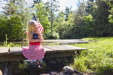 Amerikan bayrağı ile köprü üzerinde oturan gülümseyen küçük kız