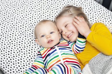 Küçük mutlu kız yatakta uzanıyor ve erkek kardeşine sarılıyor. Neşeli erkek ve kız kardeşlerin birlikte dinlenme portresi. Kardeşler, aile, çocuk bakımı