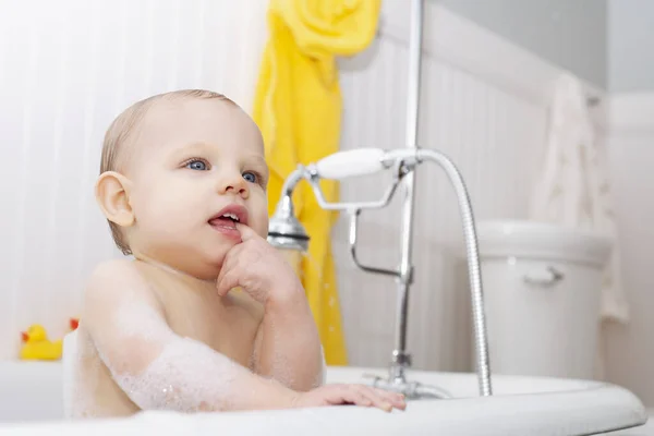 stock image Portrait of cute baby boy sitting in bathtub biting finger. Little son bathing in bathroom. Childhood, childcare, hygiene