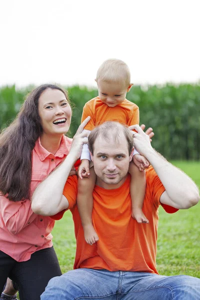 一个快乐的家庭在公园里合影的肖像 两个人坐在草地上 小男孩坐在他父亲的脖子上 — 图库照片