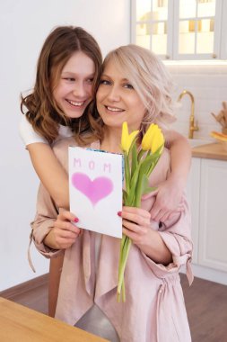 Tatilde annesini kucaklayan mutlu genç kızın portresi. Anneler Günü 'nde annemi çiçeklerle ve tebrik kartıyla tebrik eden bir kızım var. Aile, tatil, doğum günü konsepti
