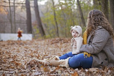 Genç bir anne oğluyla birlikte ağaçların arasında yürüyor ve manzaraya bakıyor. Sonbaharda çocukla birlikte yeşillikte oturan bir kadın. Annelik, genç anne, çocuk bakımı.