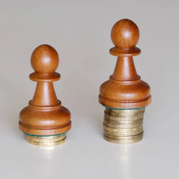 Two wood pawns chess pieces on columns of coins, symbolizing significant income inequality