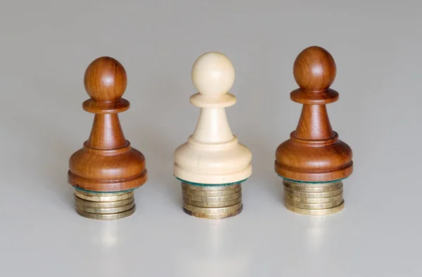 Three wood pawns chess pieces on columns of coins, symbolizing the equality of income