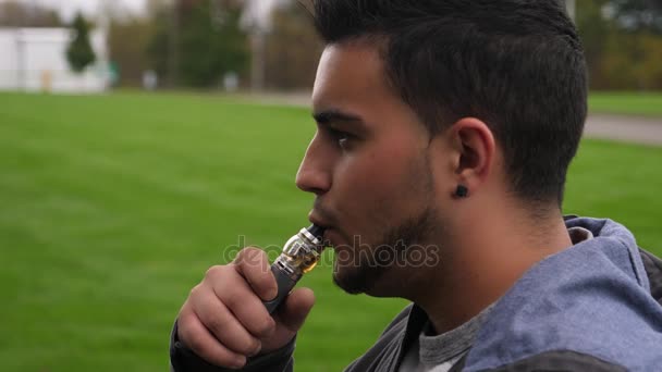 Profilbild eines Millennial-Mannes, der in Zeitlupe Rauch aus einem Vaporstift pustet — Stockvideo