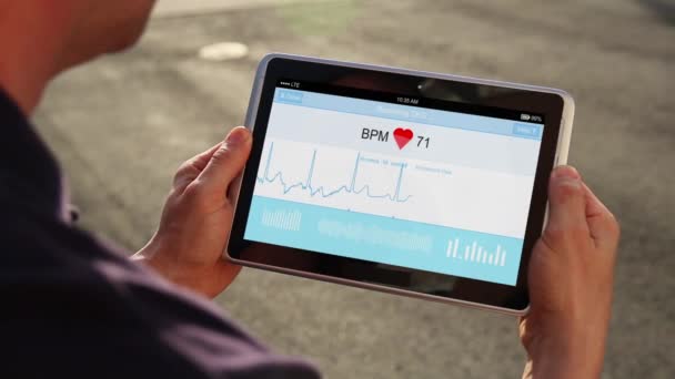Hombre sostiene dispositivo de tableta para monitorear su electrocardiograma — Vídeos de Stock