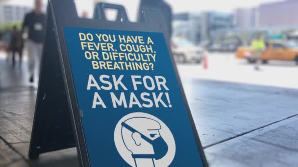 忙しい都市エリアの看板は 歩行者がコロナウイルスCovid 19の普及を助けるために顔マスクを求めることを通知します スペイン語版あり — ストック動画