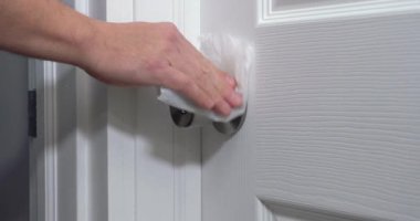 Bir adam girmeden önce kapı kolunu dezenfektanla temizliyor. 2020 Coronavirus COVID-19 salgını sırasında dezenfekte ve temizlik yüzeyleri gerekli hale geldi..  