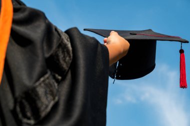 Mezuniyet şapkasını ellerinde tutan öğrenciler tören sırasında parlak bir gökyüzünde üniversiteden mezun oldular, Yüksekokulda Başarılı Eğitim Konsepti, 
