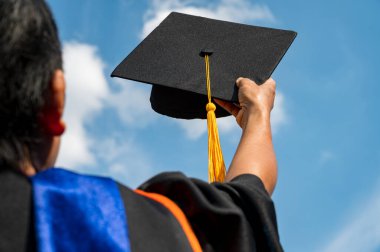 Mezuniyet şapkasını ellerinde tutan öğrenciler tören sırasında parlak bir gökyüzünde üniversiteden mezun oldular, Yüksekokulda Başarılı Eğitim Konsepti, 