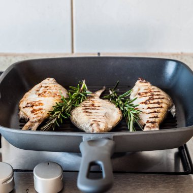 Gaz ocağının tepesindeki tavada ızgara Breams, kare.