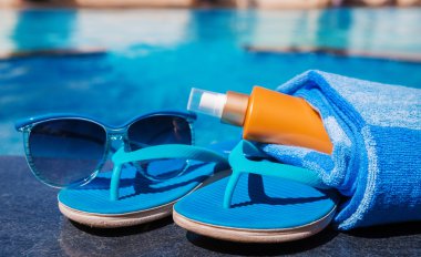 Güneş koruyucu krem, mavi terlik ve havlu bord üzerinde güneş gözlüğü