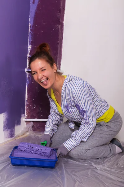Ung attraktiv kvinna målar vit vägg med lila färg rolle — Stockfoto