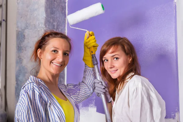 Kvinnor målar vit vägg med lila färg roller — Stockfoto