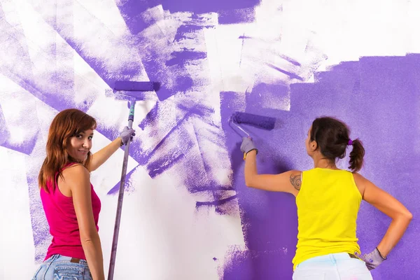 women paints white wall with purple paint roller