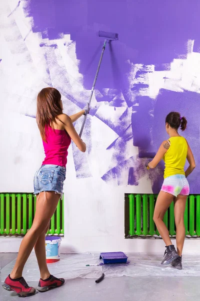 women paints white wall with purple paint roller