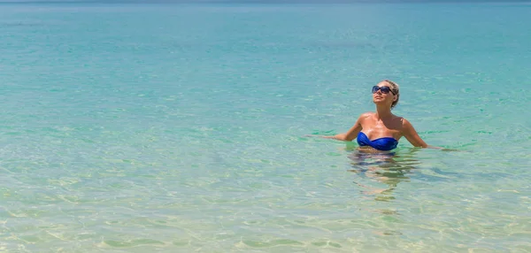Schlanke blonde Frau schwimmt am tropischen Strand — Stockfoto