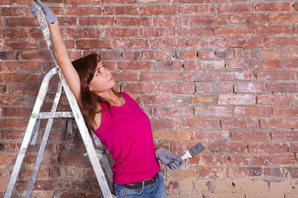 Kvinna målare på en stege nära tegelvägg — Stockfoto