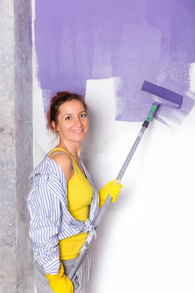 Kvinna målar vit vägg med lila färg roller — Stockfoto