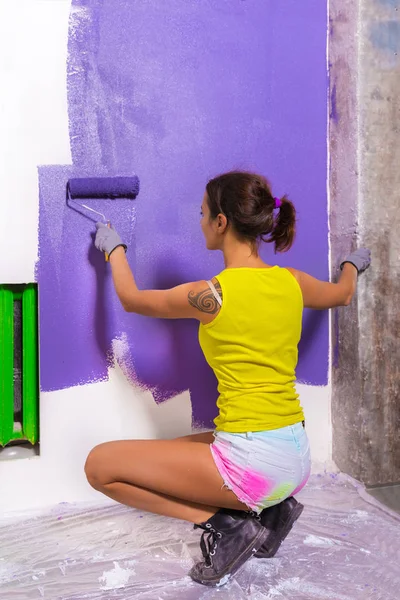 attractive woman paints white wall purple roller