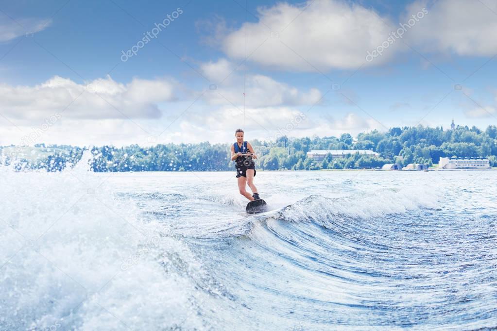 slim woman riding wakeboard on wave of boat