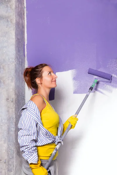 Kvinna målar vit vägg med lila färg roller — Stockfoto