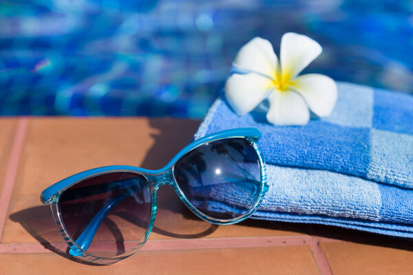 Fluffy towel with sunglasses and flower on border of a swimming 